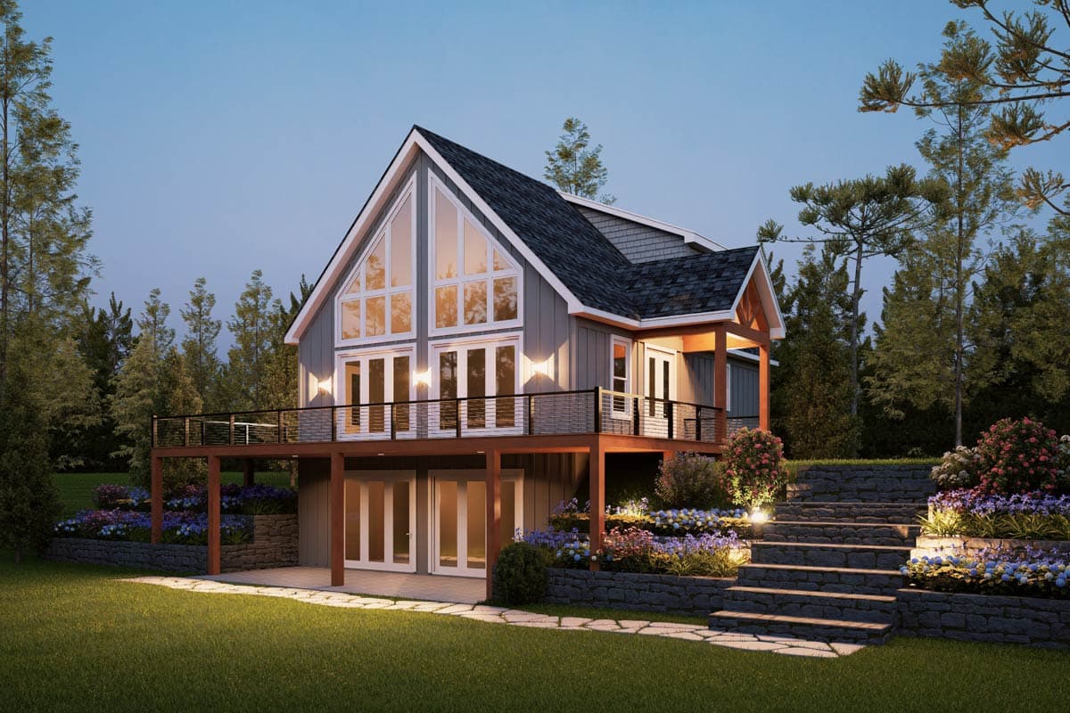 A modern two-story home with a large triangular window, a wraparound deck, and a terraced garden with blooming flowers and stone steps.