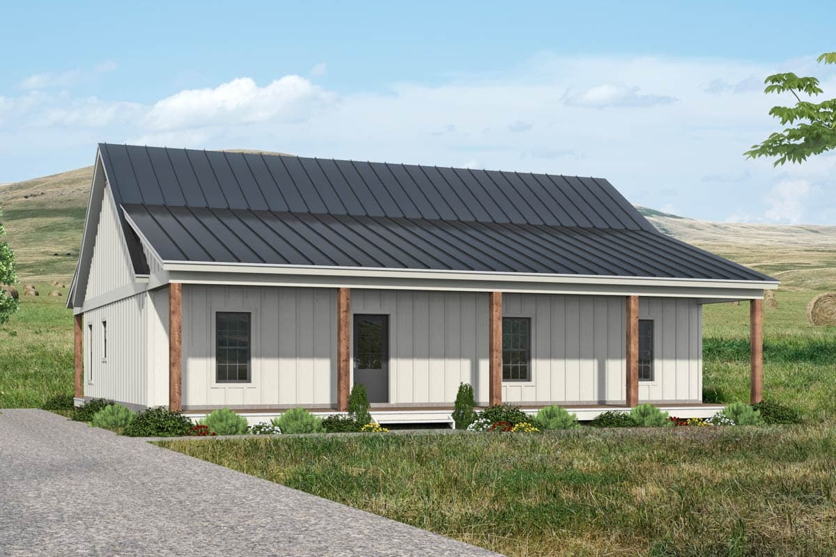 A white farmhouse with a dark gray metal roof and a porch supported by wooden columns sits in a grassy field on a sunny day.