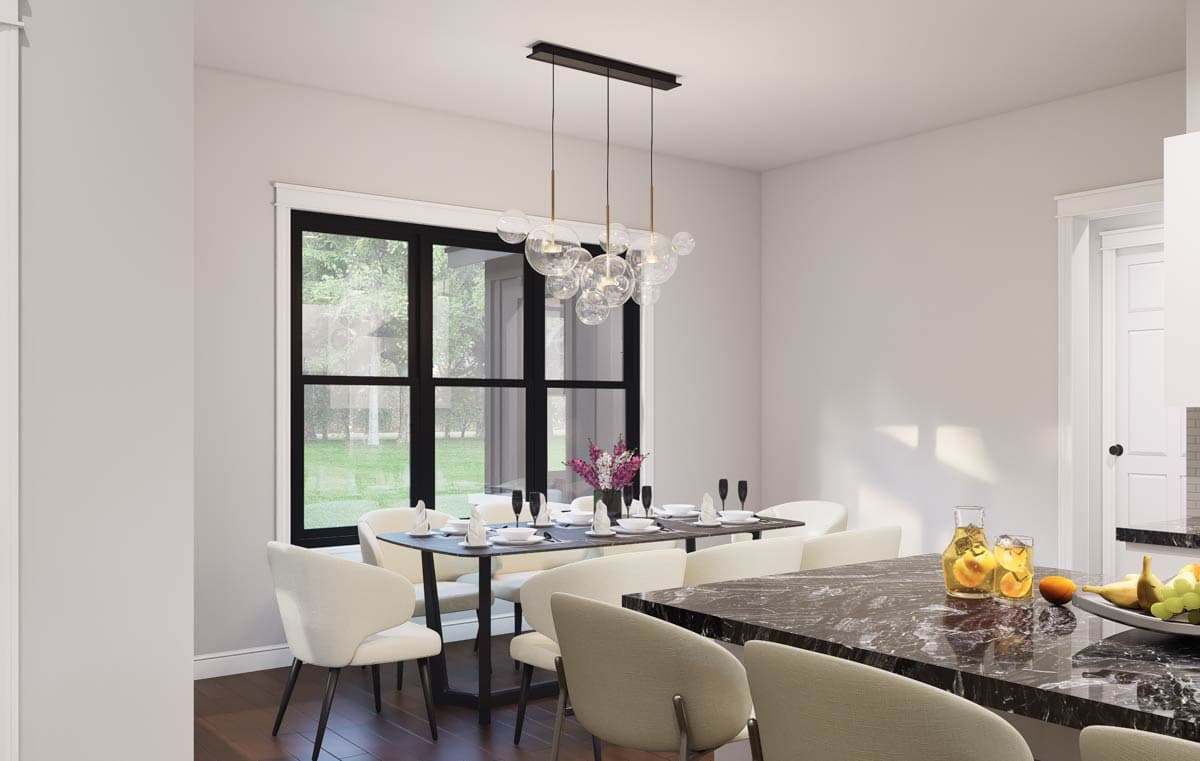 Dining area with a long table set for dinner, minimalist chandelier, and large window overlooking a lawn.
