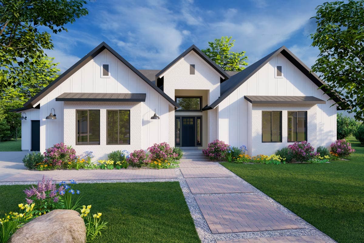 A modern white house with a black roof, a brick walkway, and a landscaped front yard with colorful flowers under a bright blue sky.