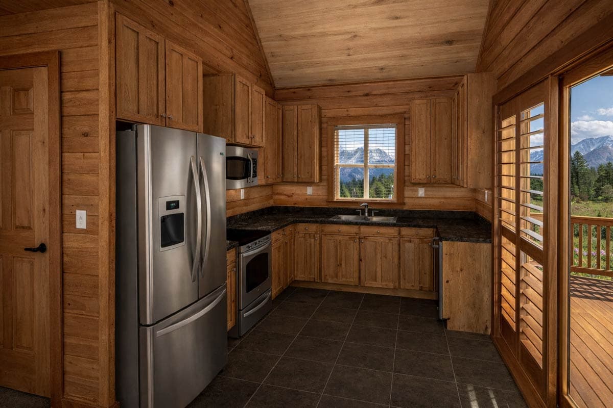 Log cabin kitchen interior with stainless steel appliances, wood cabinetry, granite counters, and large window with mountain view.