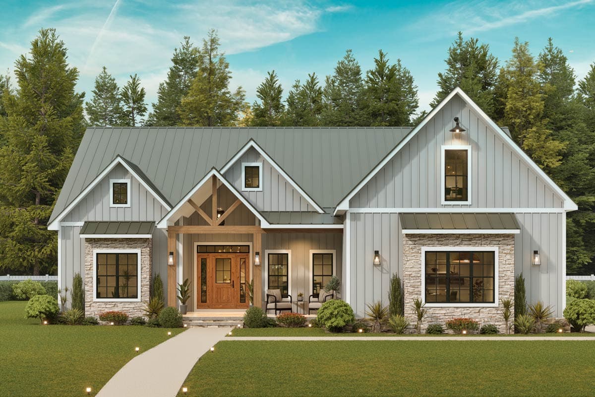 A modern farmhouse with a gray exterior, stone accents, and a wooden front door. A pathway leads to the entrance surrounded by a green lawn and trees.