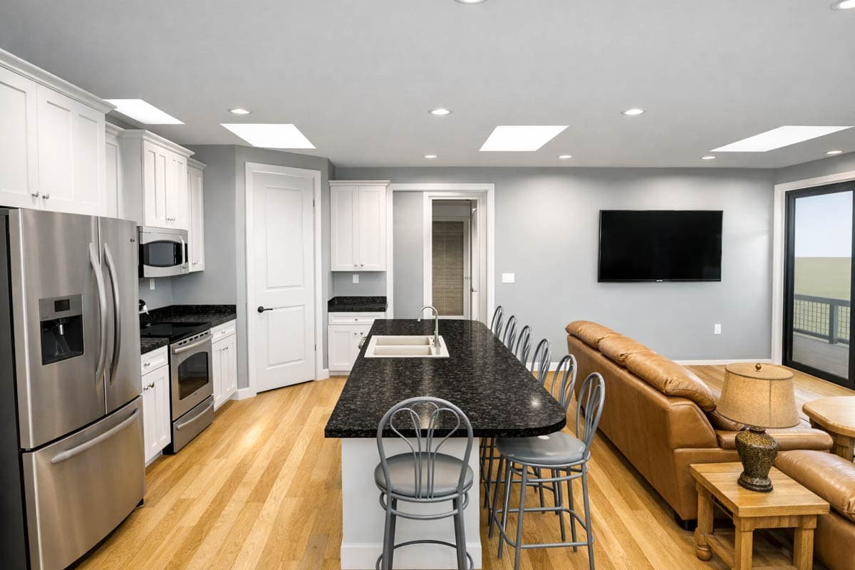 Open-concept kitchen and great room with a large island, seating for four, stainless steel appliances, and a leather sofa.