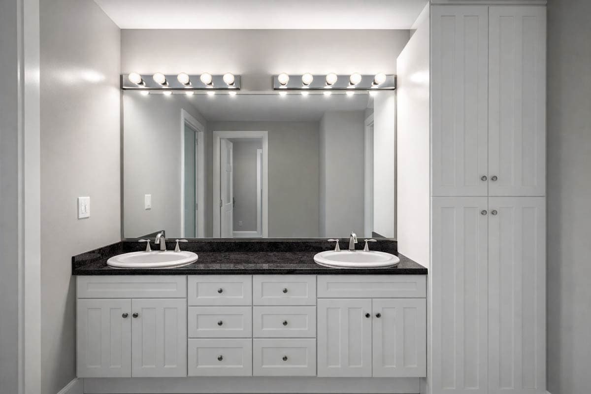 Bathroom with double vanity, granite countertop, vanity lights, and a tall linen cabinet.