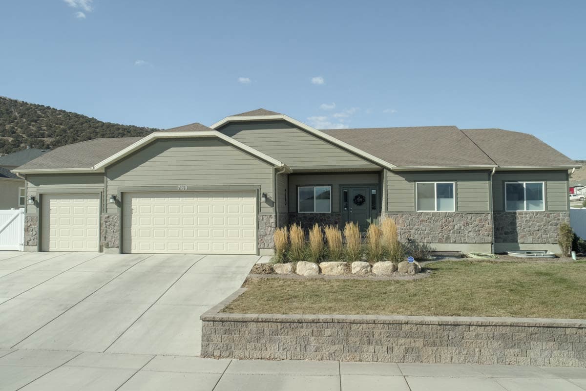 House plan exterior. Ranch style, single story home with a two-car garage, stone facade, and a gabled roof.