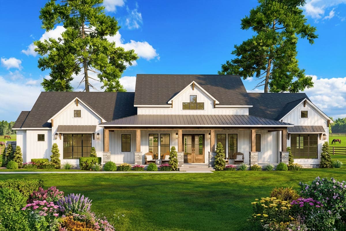 A large, white farmhouse with a wraparound porch, set on a lush green lawn. Two tall trees flank the house, with a blue sky overhead.