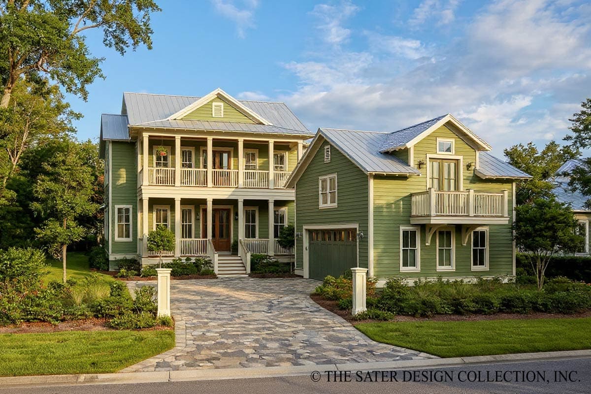 Two-story green house with a porch and a detached garage, both with silver roofs. A stone paver driveway leads to the house.