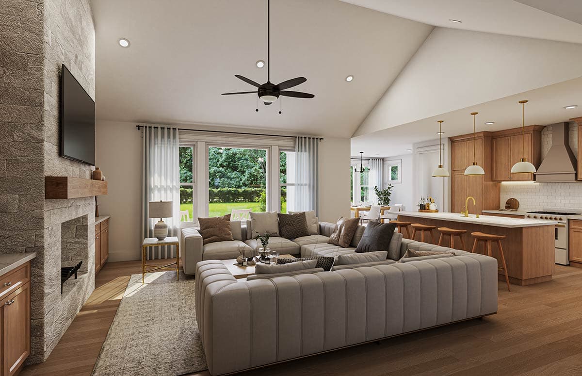 Interior view of a great room with stone fireplace, sectional sofa, vaulted ceiling, and open kitchen with island.