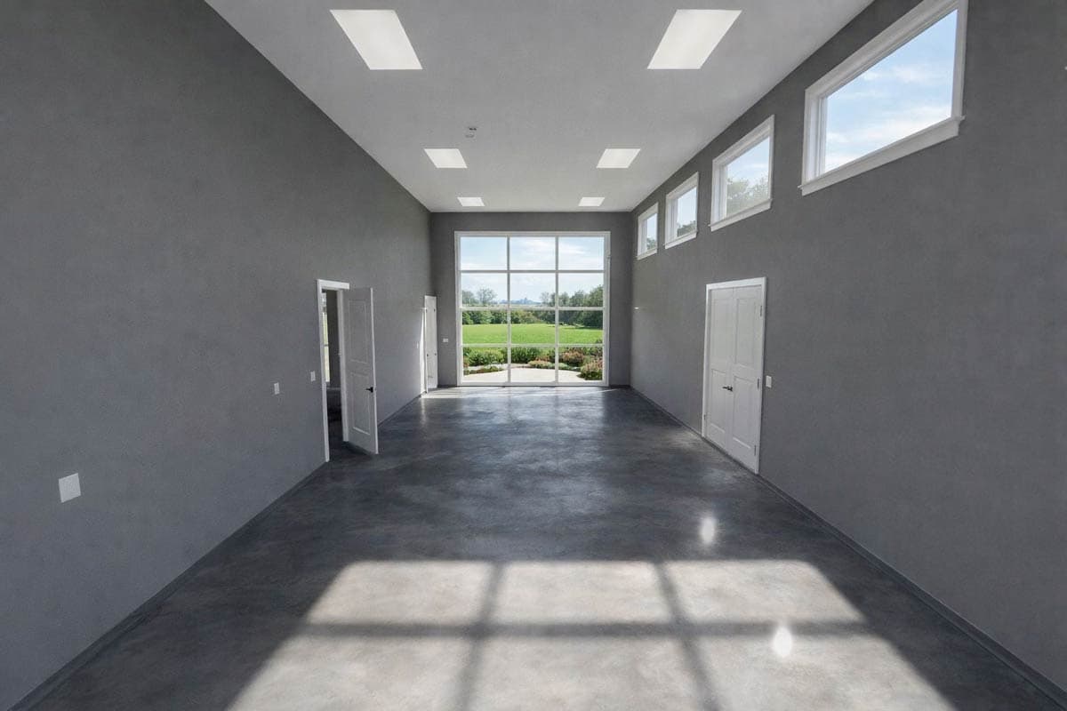 Interior view of large room with gray walls, polished concrete floor, skylights, and large windows overlooking a green landscape.
