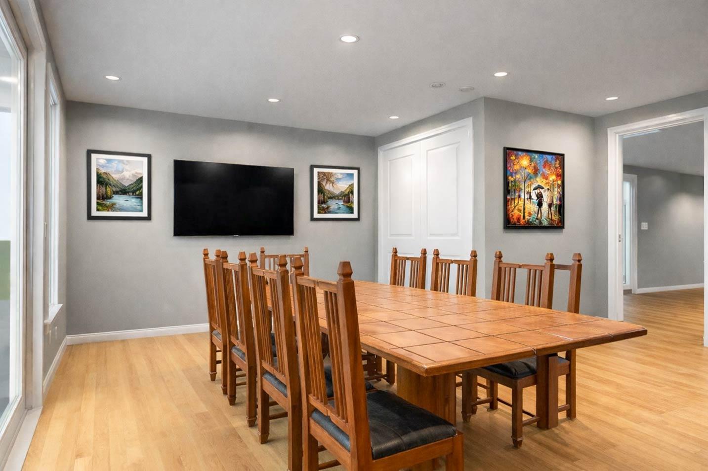 Dining room with wood table, chairs, flat-screen TV, large windows, and artwork.