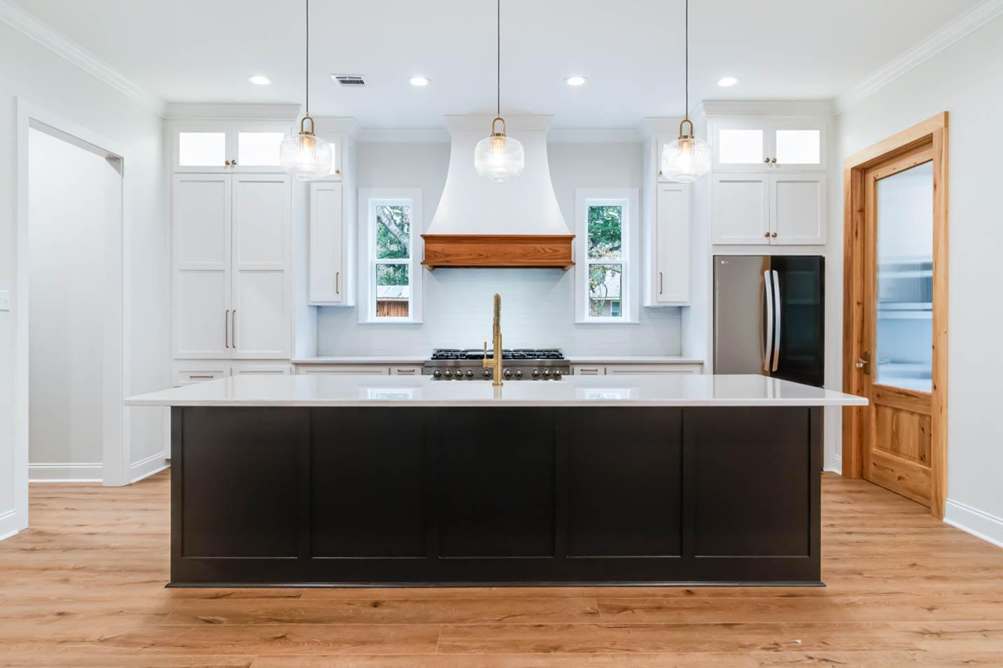 Modern kitchen with dark island, white shaker cabinets, range, and natural wood door.