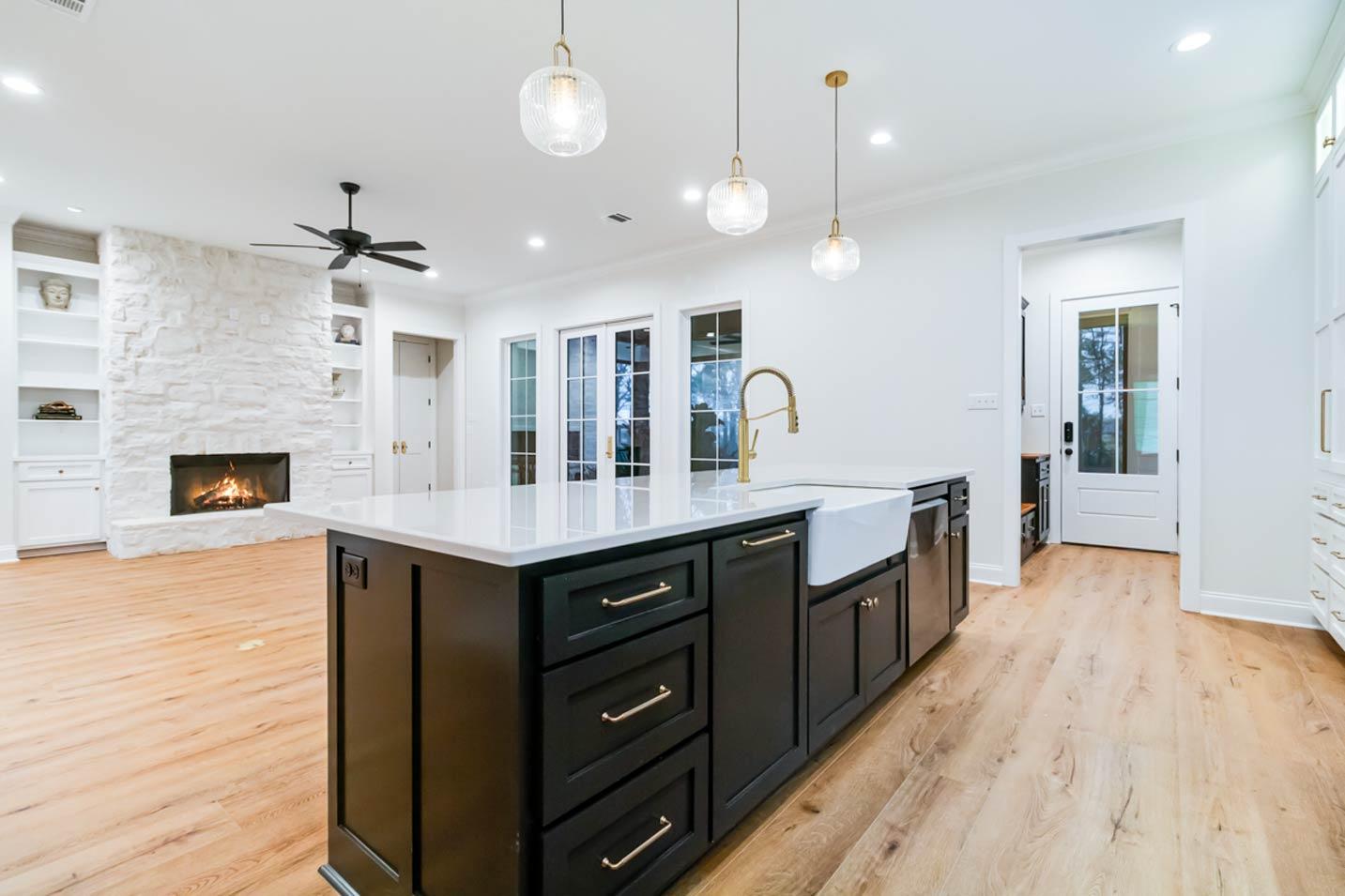 Open concept kitchen and living area with a large stone fireplace, island with sink and faucet, and double doors.