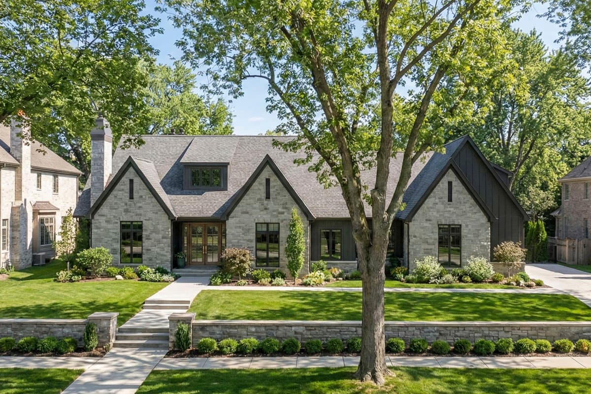 House plan exterior. Stone and dark-siding facade with gabled roof, dormers, and stone chimney. Features include a front porch and a landscaped yard.