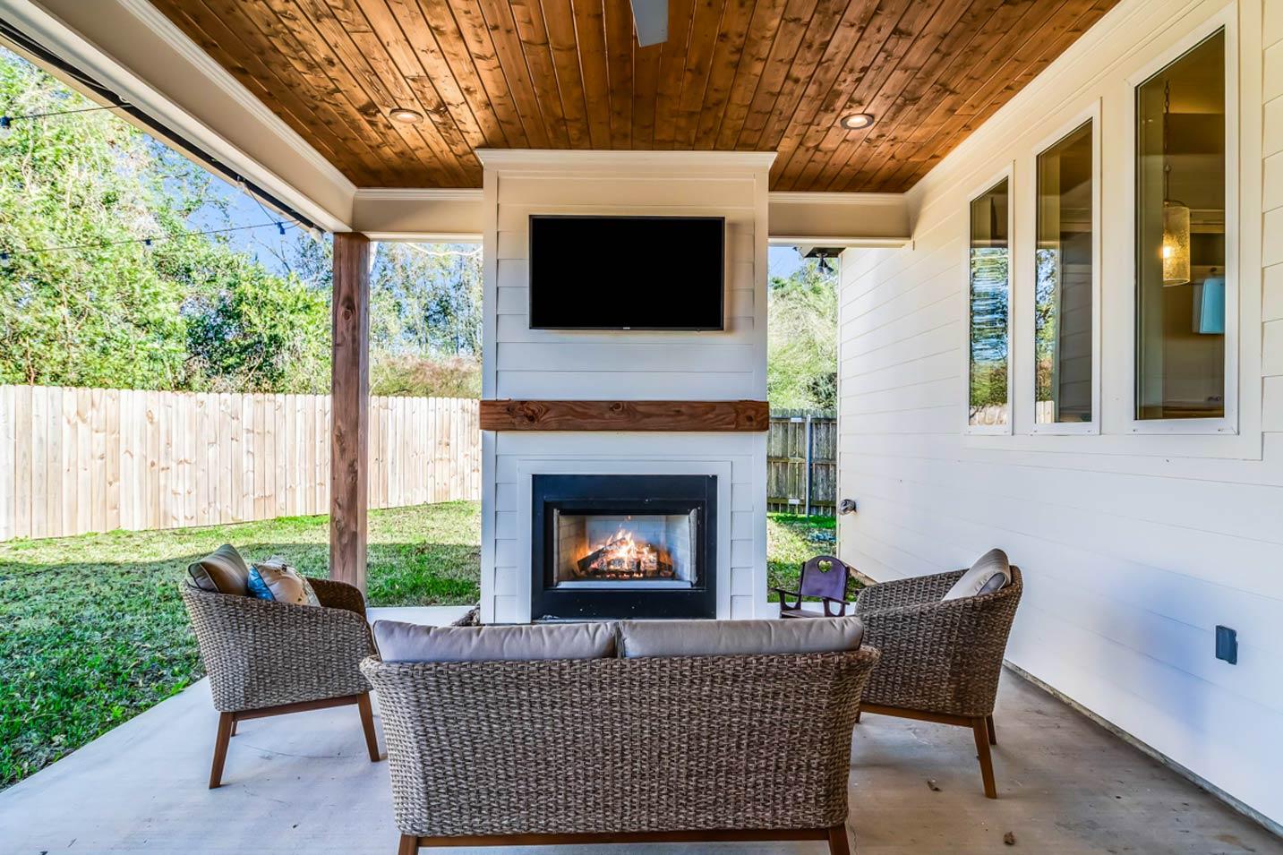 Covered patio with fireplace, television, wood-paneled ceiling, and seating area.