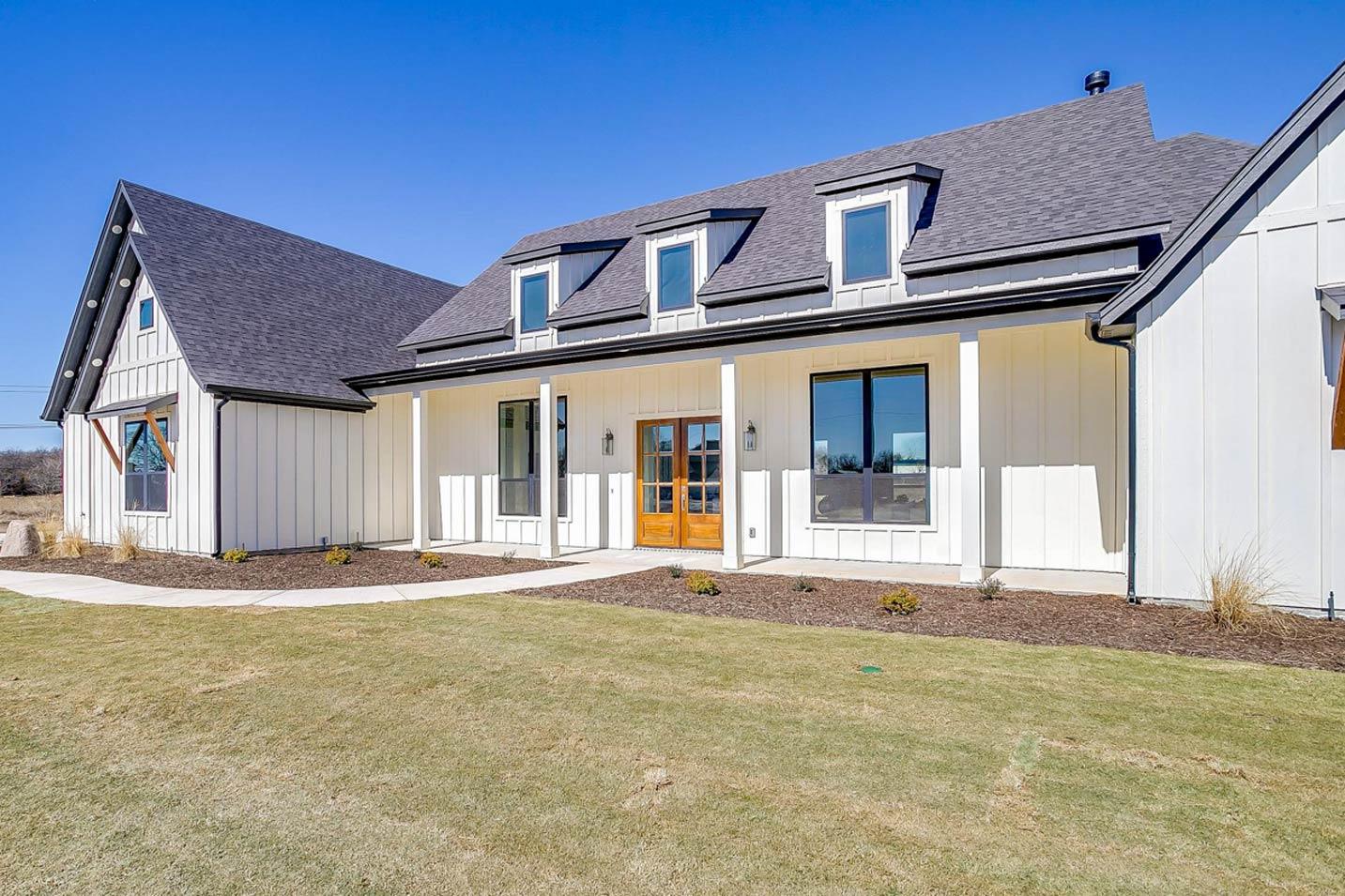 Modern Farmhouse exterior with white board-and-batten siding, covered porch, dormer windows, and steep gable.