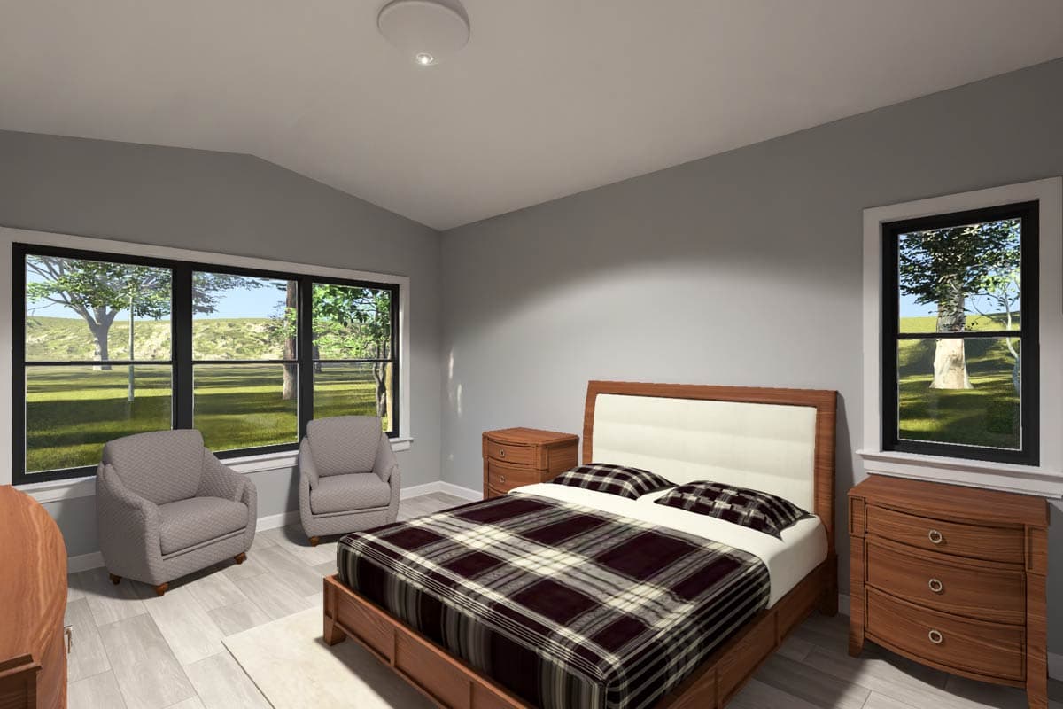 Bedroom with vaulted ceiling, king-size bed, two chairs, and large windows overlooking a grassy landscape.