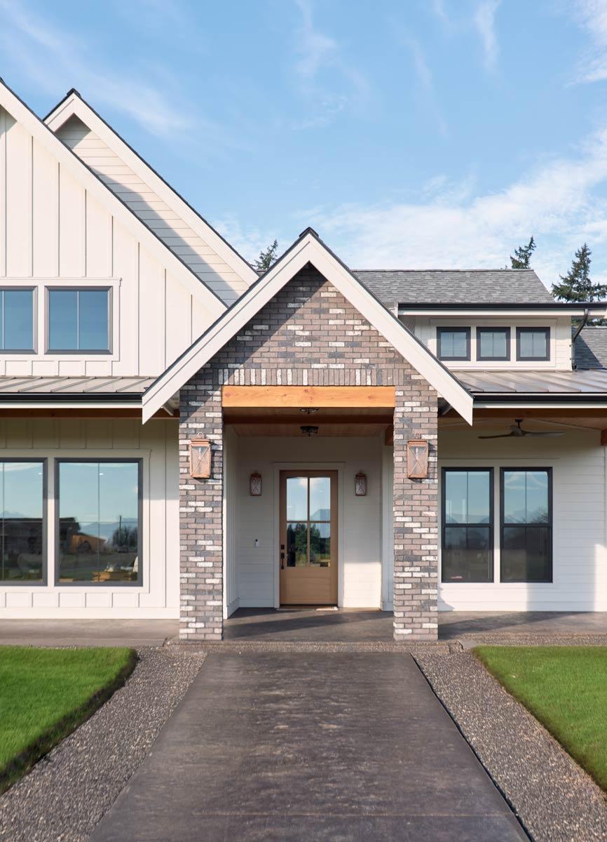 Modern Farmhouse house plan exterior with white board and batten siding, brick accents, gabled roofline, and wood beam entry.