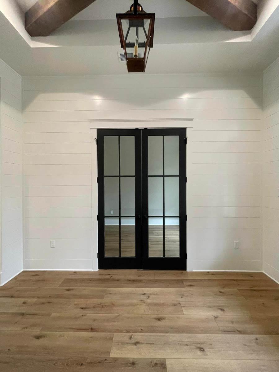 Interior view of room with shiplap walls, wood-look flooring, tray ceiling with wood beams, and double glass doors.
