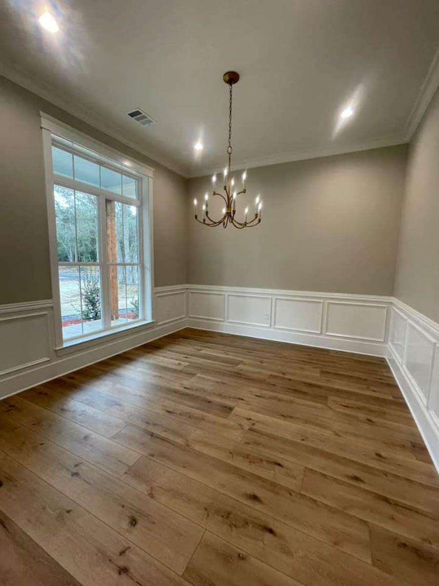 Dining room with large window, wainscoting, chandelier, and wood-look flooring.