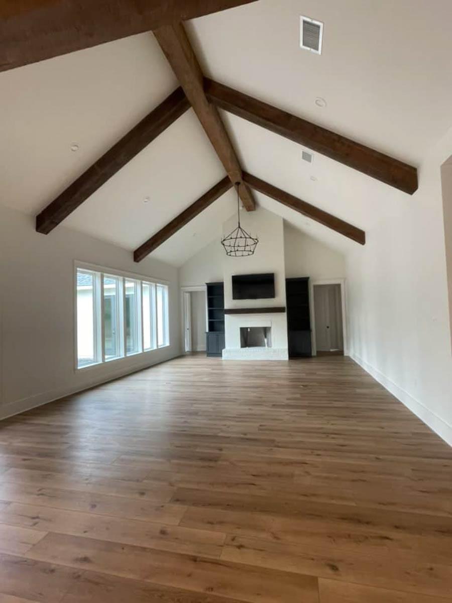 Great room interior with vaulted ceiling, exposed wooden beams, fireplace, and large windows.