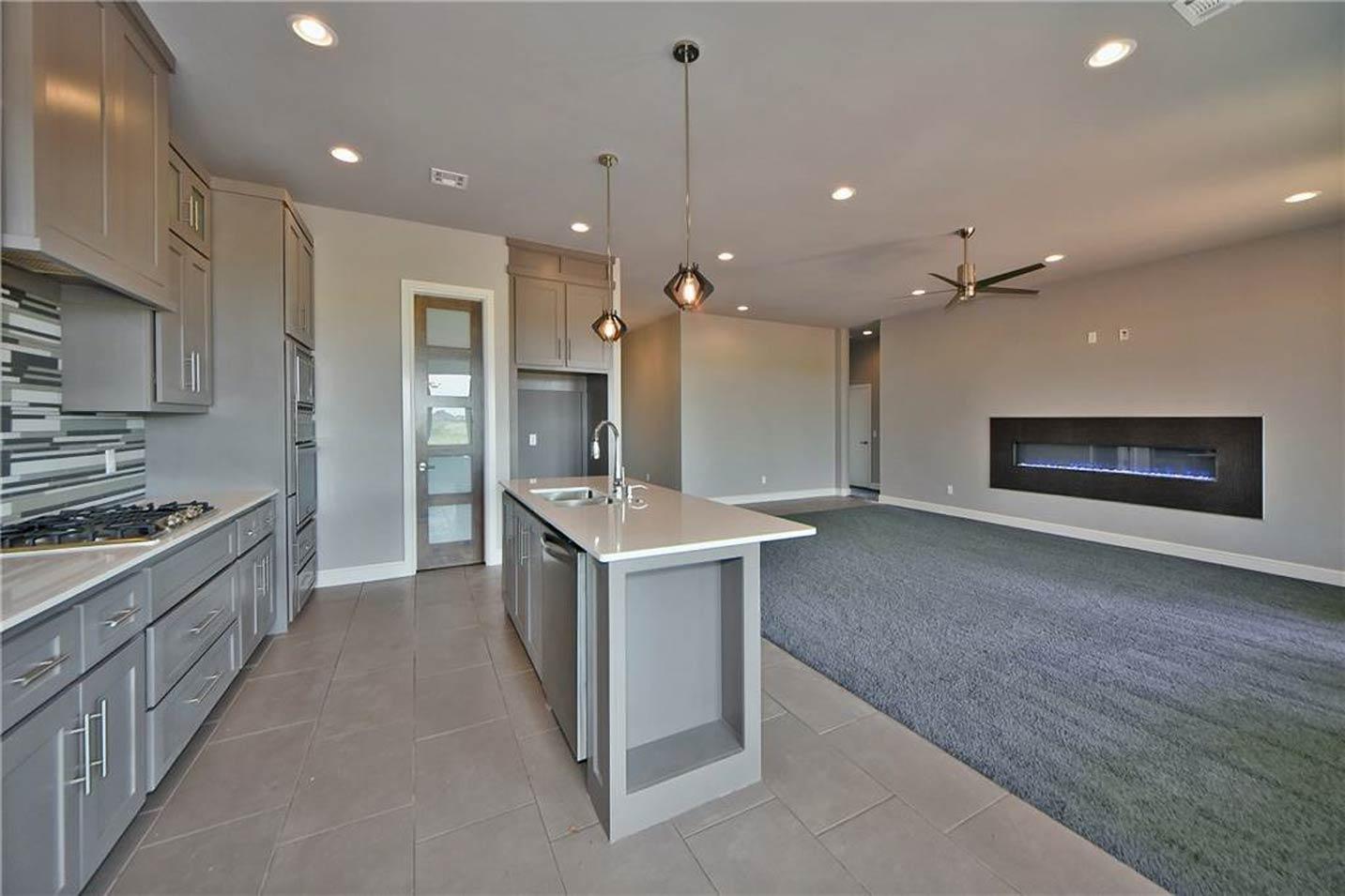 Modern open-concept living space with a grey kitchen island, linear fireplace, and vaulted ceiling.