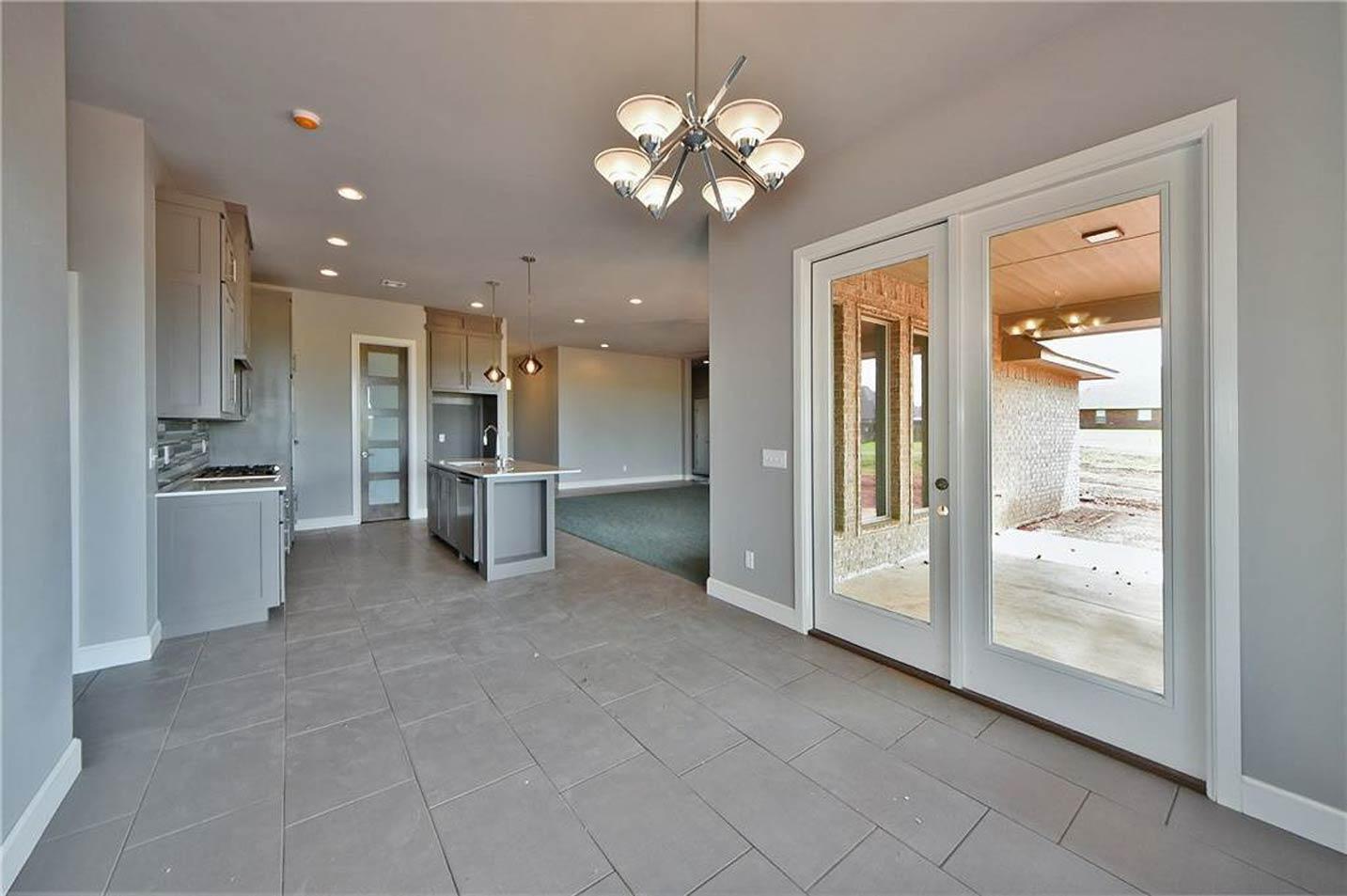 Kitchen with gray cabinets, island with sink, and double doors leading to an outdoor patio. Open view to living area.