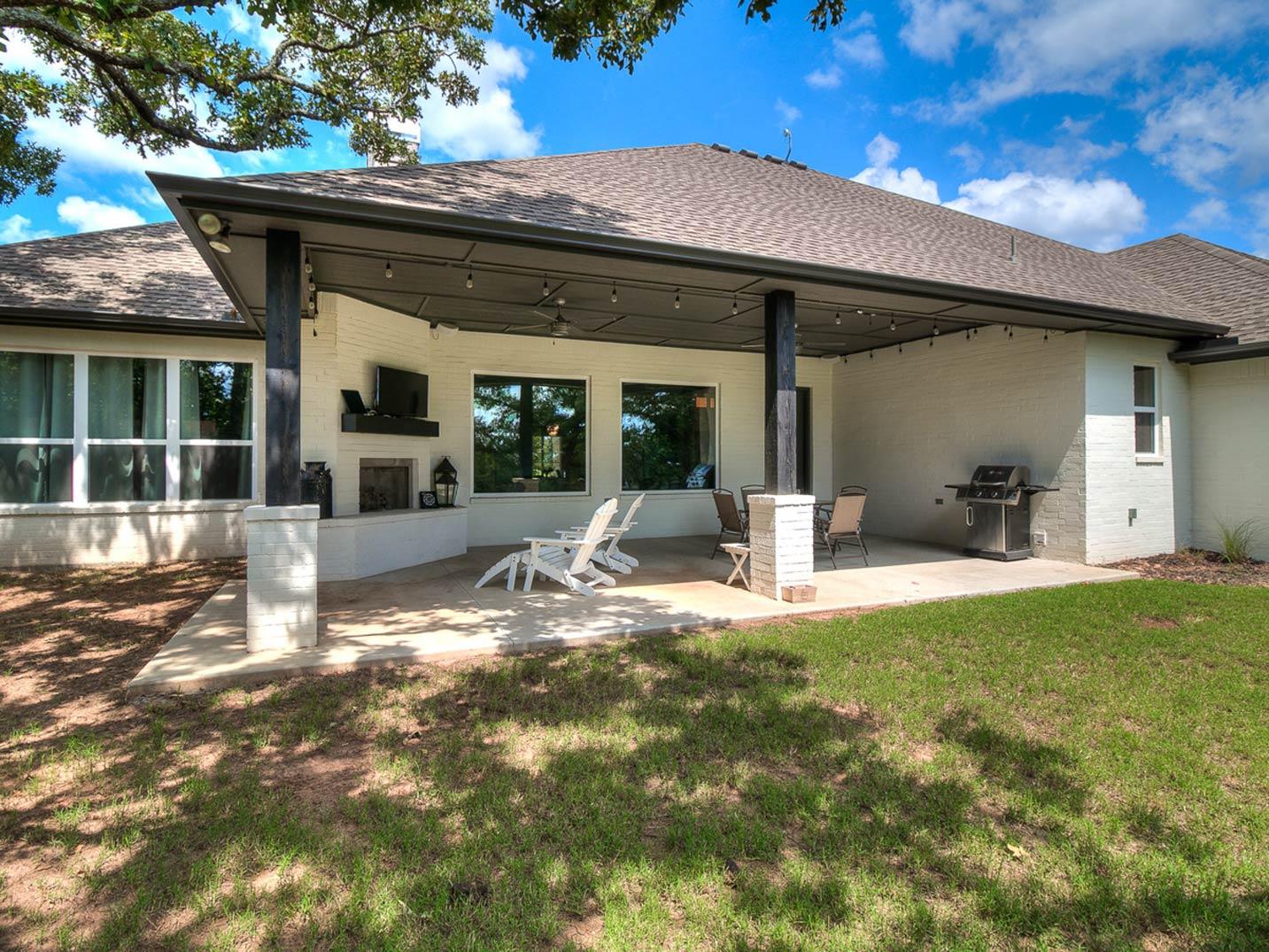 Modern house exterior with covered patio, outdoor fireplace, grill, and seating area.