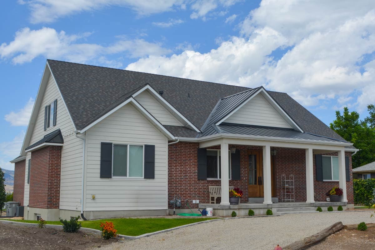 House plan exterior: Modern Farmhouse style, one and a half stories, brick and vinyl siding, prominent gables, and covered front porch.