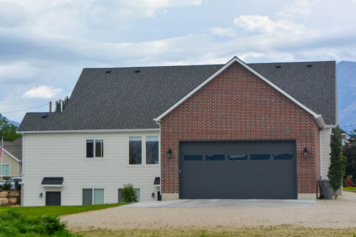 Two-story house plan exterior with white siding, red brick garage, and dark roof.