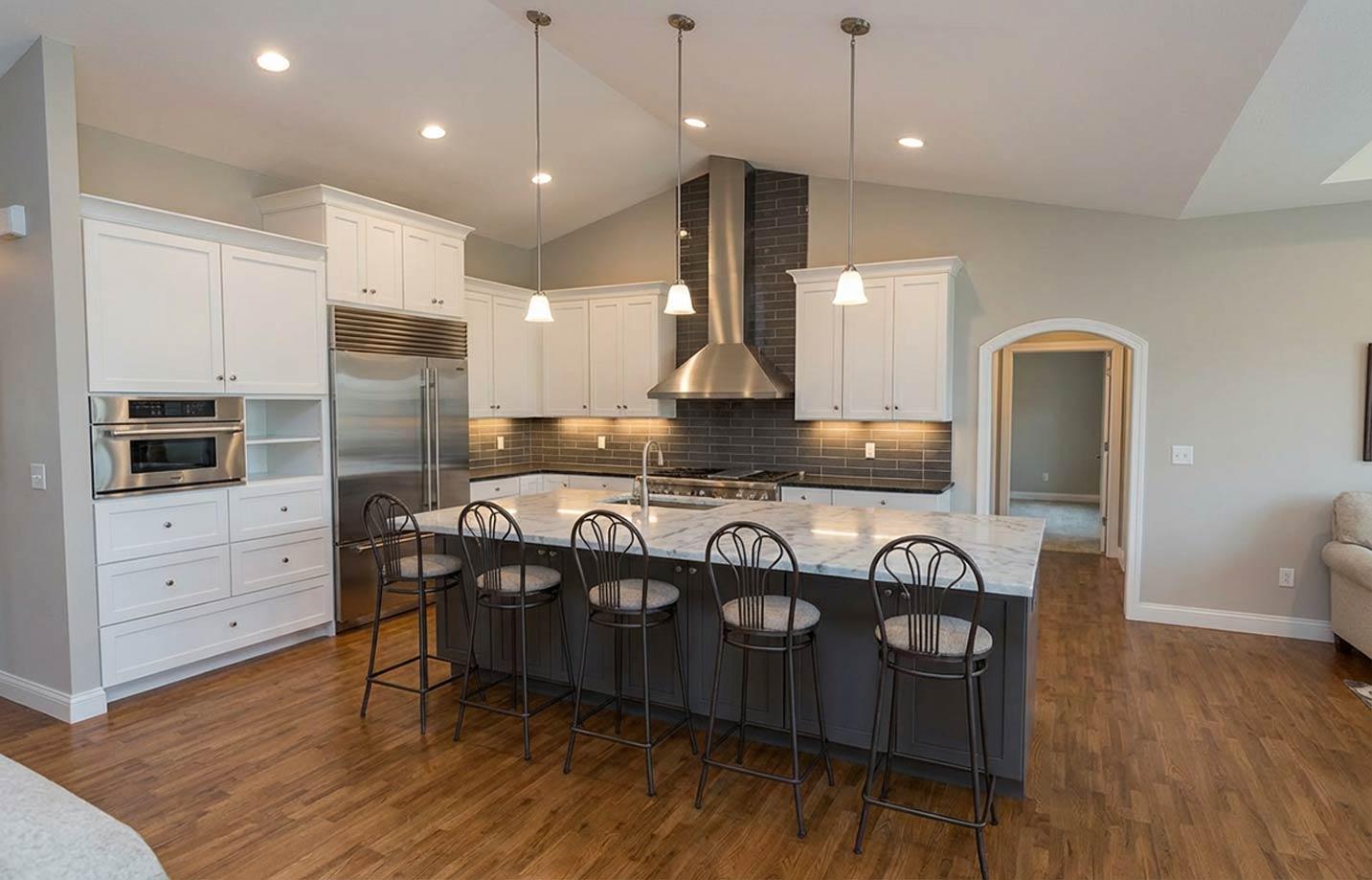 Kitchen interior with white cabinets, large island with marble countertop, stainless steel appliances, and vaulted ceiling.