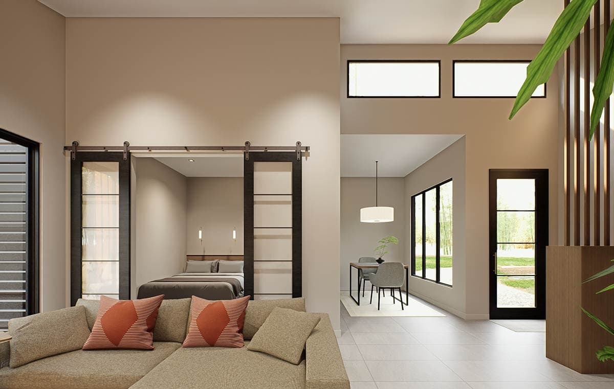Interior view of a modern living space with a sectional sofa, barn door leading to a bedroom, and dining area with large windows.