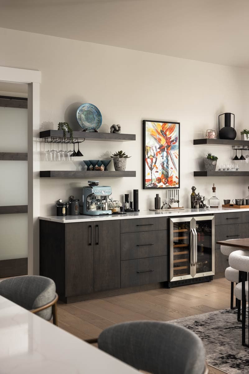 Wet bar with dark wood cabinets, white countertop, wine fridge, espresso machine, and floating shelves with stemware.