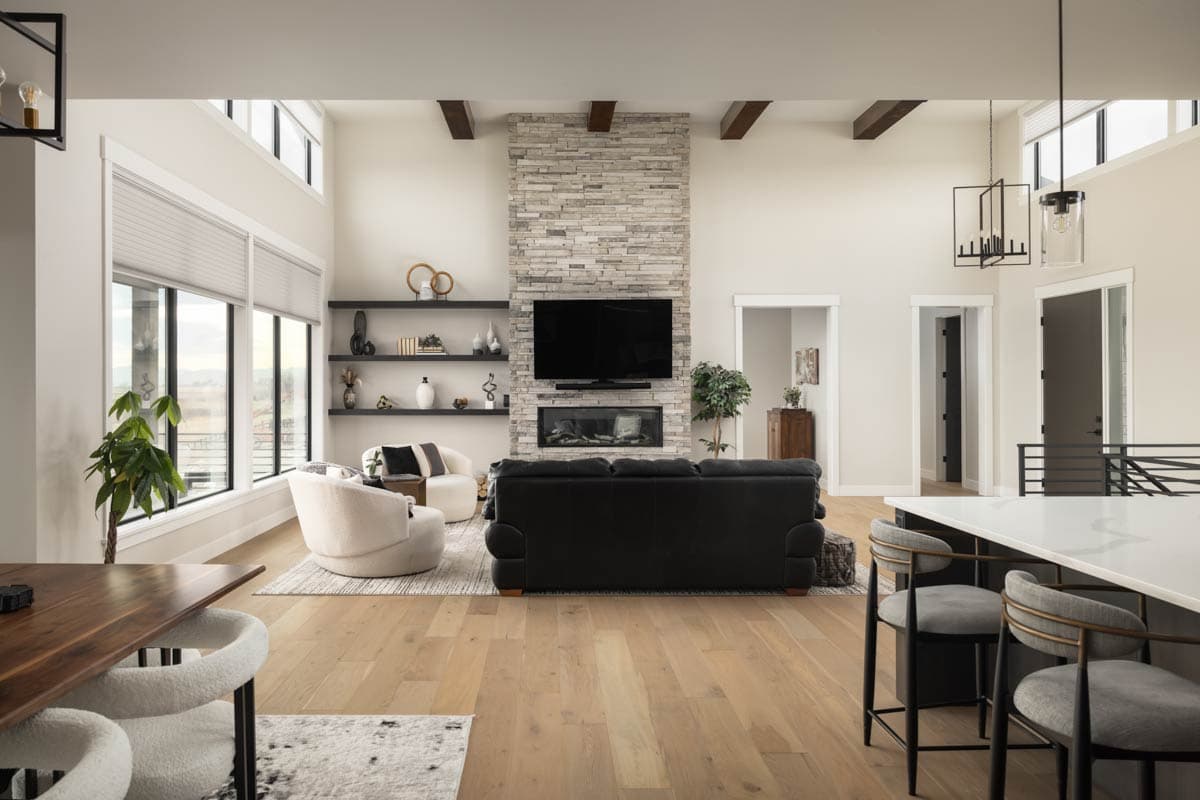 Great room interior with stone fireplace, vaulted ceiling with wood beams, and large windows.
