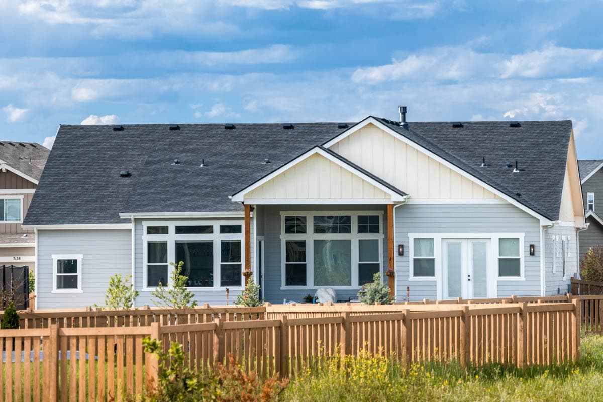 House plan exterior: Light blue siding, gray roof, white gables, covered porch with wood columns, and numerous windows.