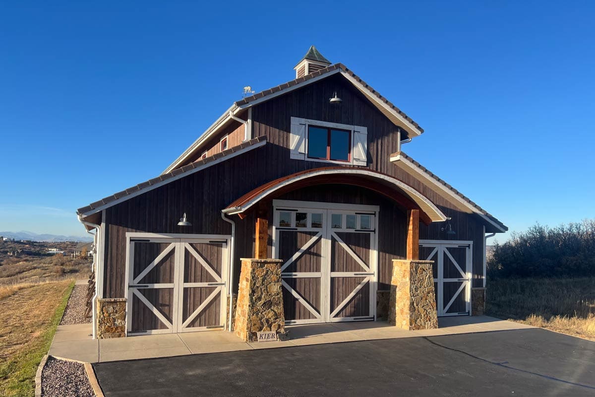 Modern barn-style house plan exterior with three garage doors, stone accents, and a curved roof entrance.
