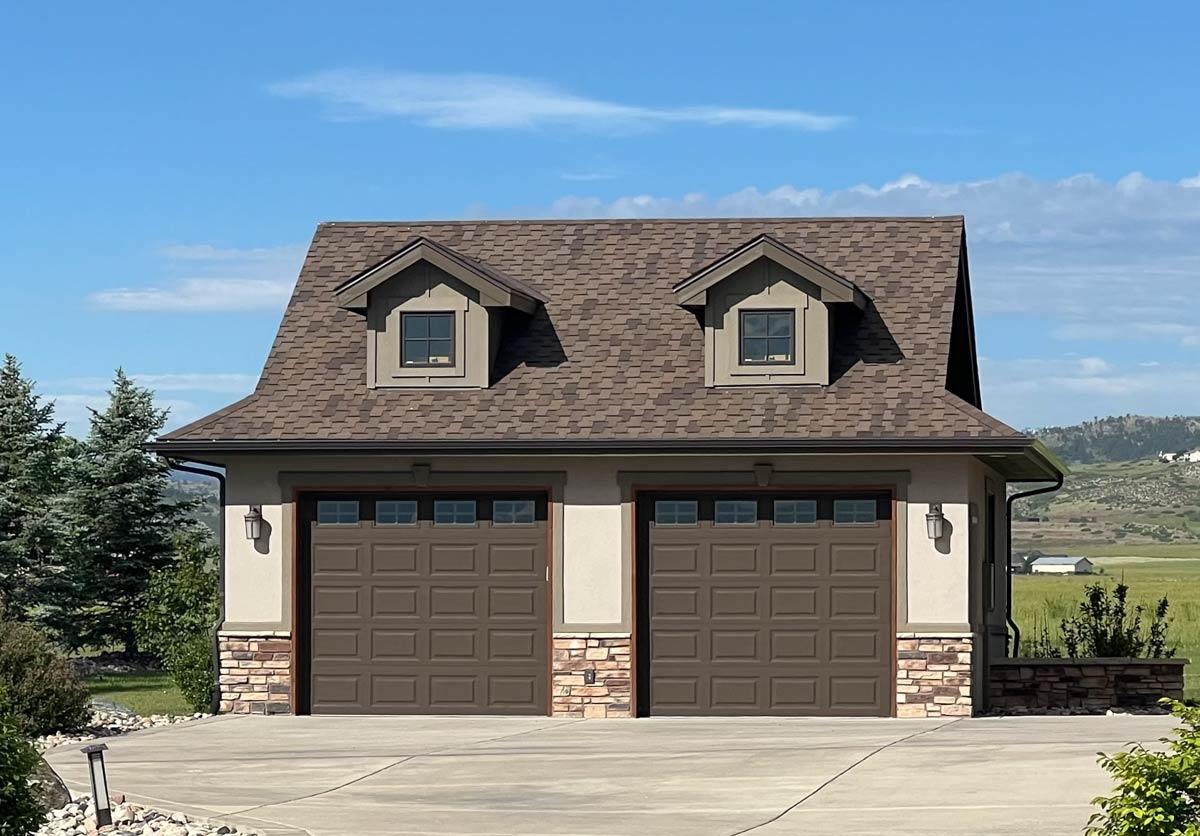 House plan exterior: Two-story garage with gable dormers, stone wainscoting, and dark brown paneled doors with glass transoms.