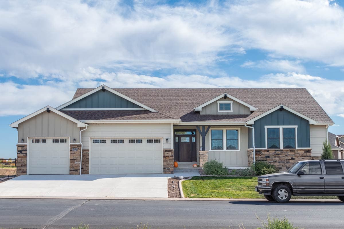 House plan exterior: Ranch style, three-car garage, stone accents, gabled dormers, and a covered entryway with wooden beams.