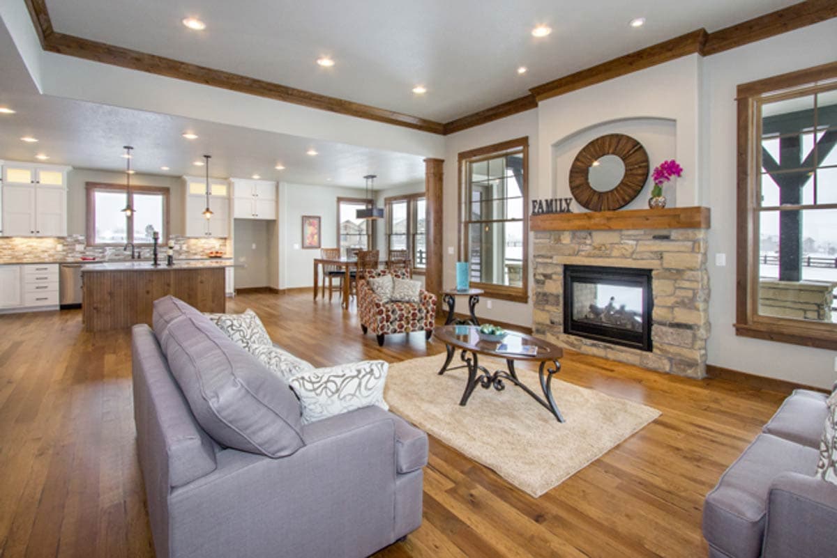 Interior rendering of a great room with stone fireplace, island kitchen, and dining area. Exposed wood beams accent the ceiling.