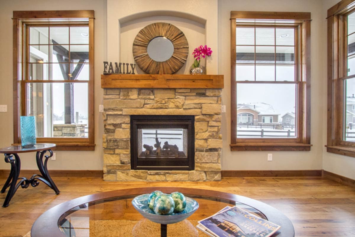 Living room interior with stone fireplace, wood mantel, and large double-hung windows.