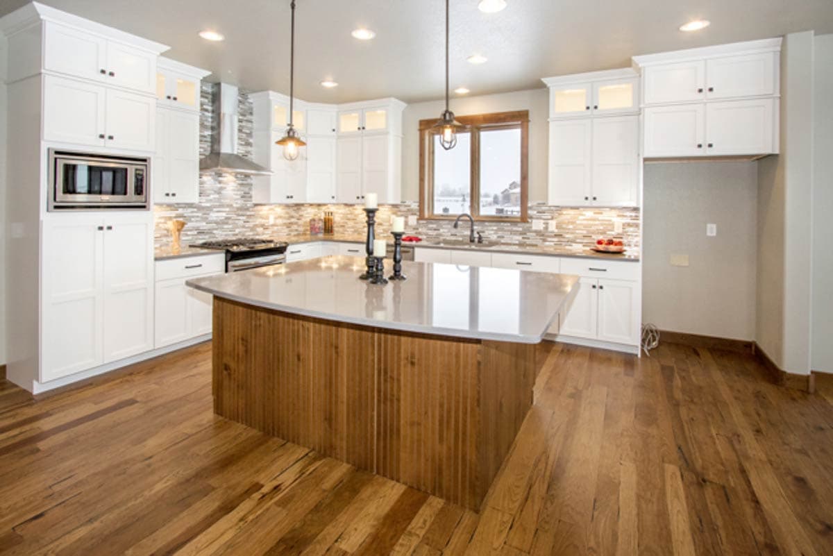 Kitchen interior with white cabinetry, a large island with wood paneling, mosaic tile backsplash, and stainless steel appliances.