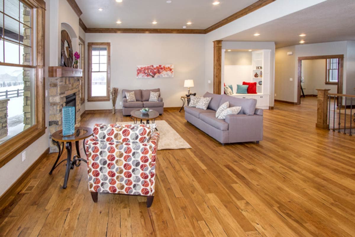 Living room interior with stone fireplace, wood beams, built-in shelving, and hardwood floors.
