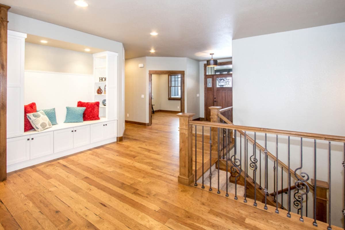 Interior view of a house entrance hall with wood flooring, built-in bench seating, and a staircase with decorative metal balusters.