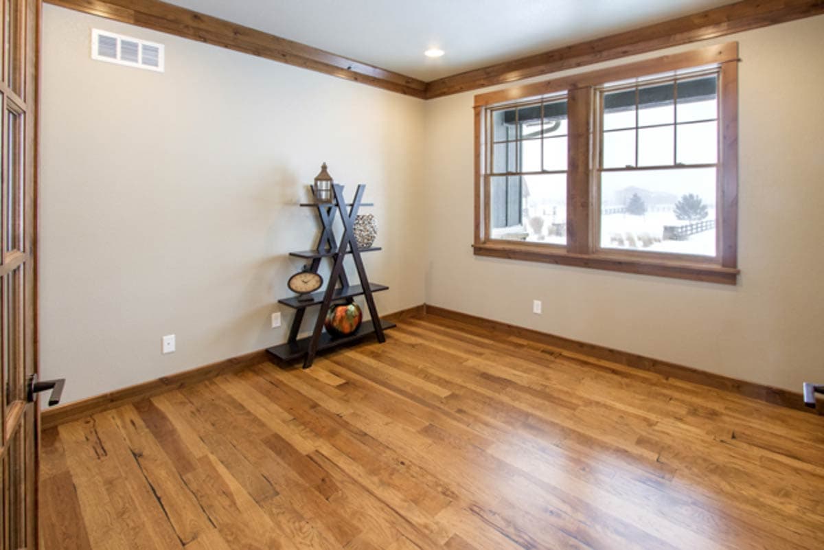 Interior view of a room with hardwood floors, wood trim, and two large windows overlooking a snowy landscape.