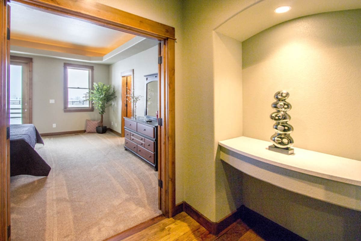 Interior view of bedroom with tray ceiling, dresser and doorway to hallway with built-in shelf.