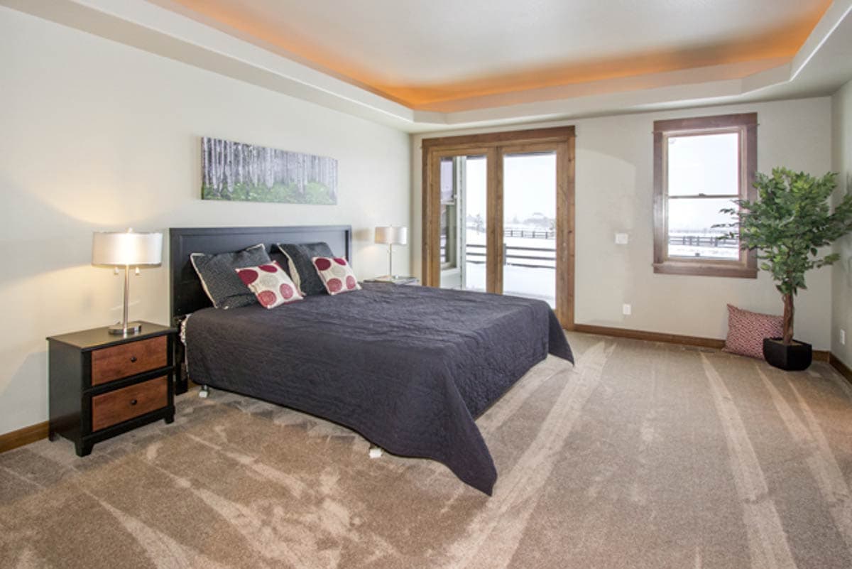 Bedroom with king bed, tray ceiling with cove lighting, and double glass doors to exterior.