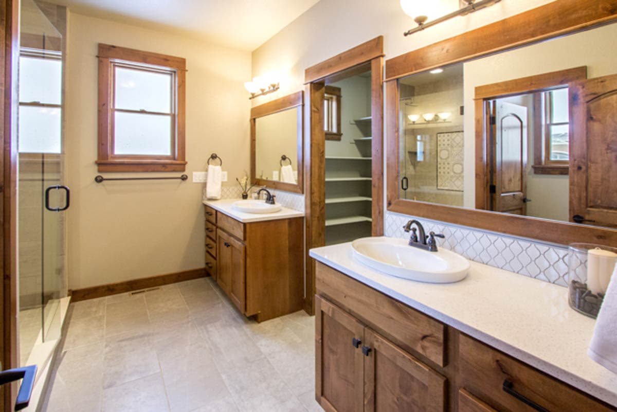 Bathroom with double vanity, walk-in closet, and glass-enclosed shower with wood trim.