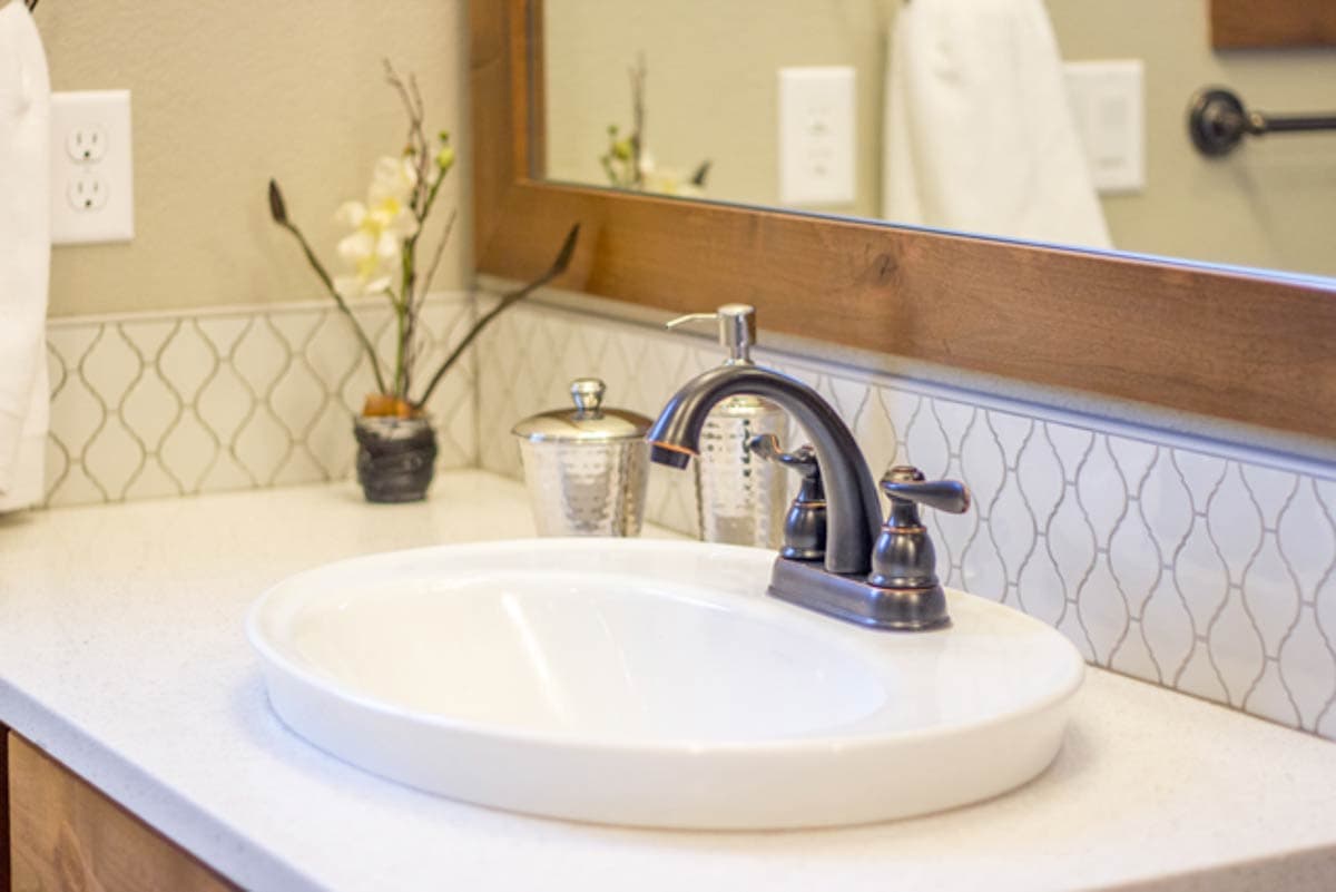 Bathroom vanity with white undermount sink, oil-rubbed bronze faucet, and decorative tile backsplash.