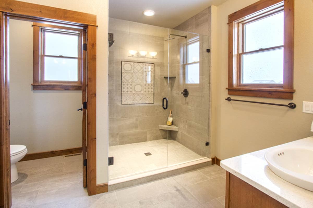 Modern bathroom with glass-enclosed tile shower, toilet, and vanity with sink.