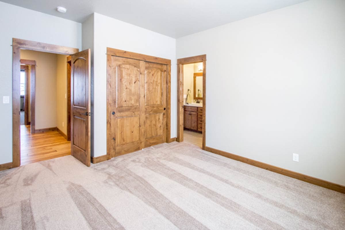 Interior view of a bedroom with a closet, an open door to a hallway, and an open doorway to a bathroom with a vanity.