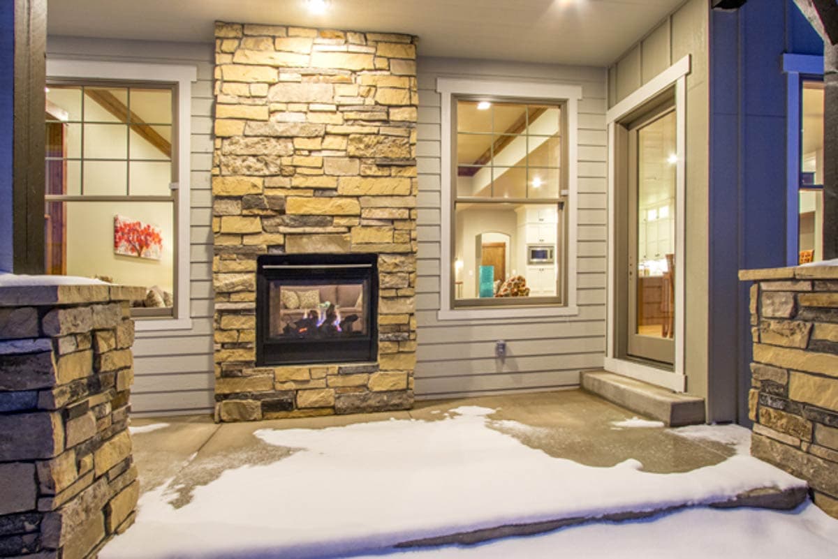 House exterior featuring a stone fireplace, siding, and windows overlooking an interior.